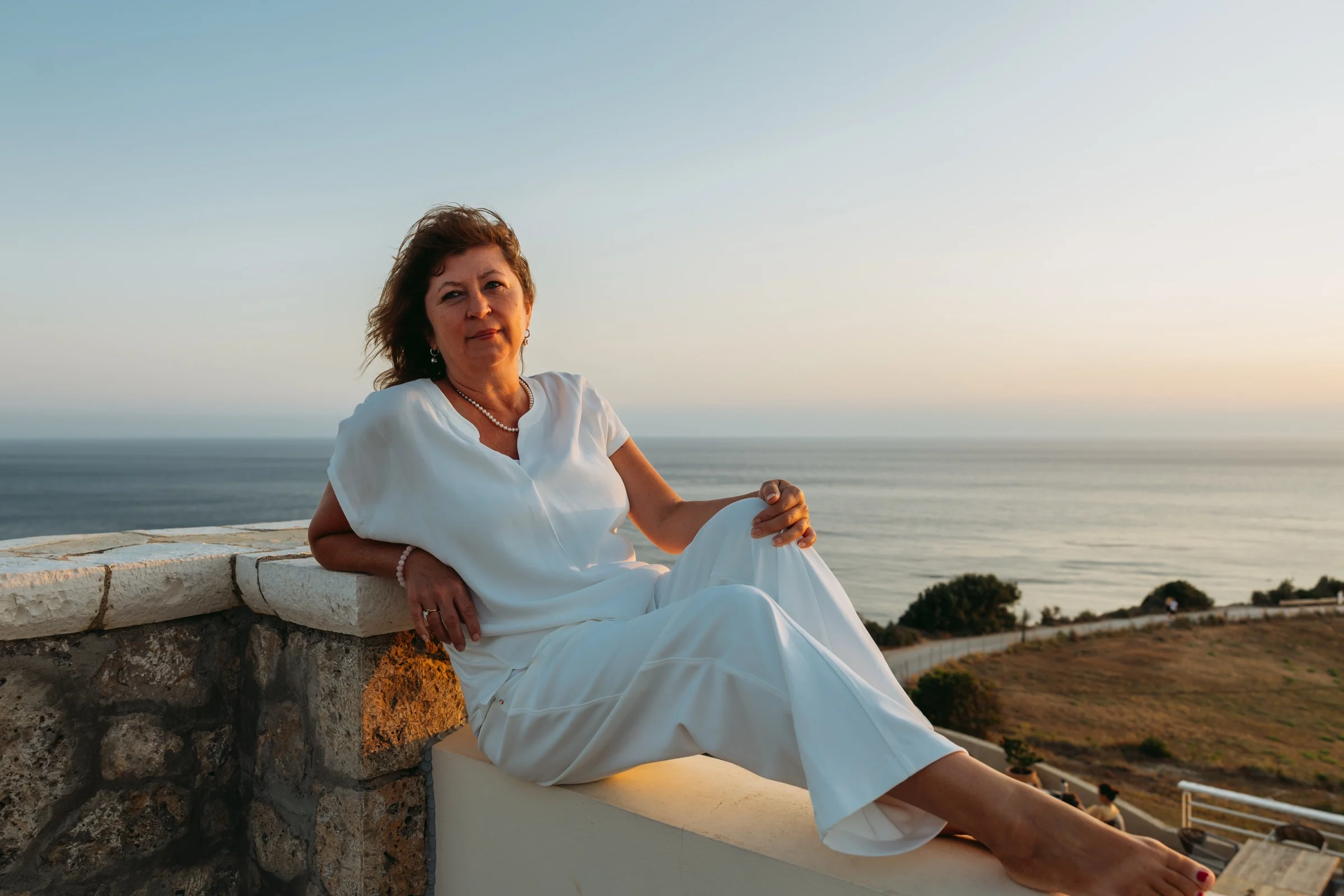 Olga Westerveld, sitzend auf einer Mauer am Meer im Abendlicht